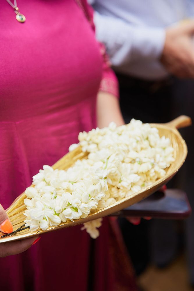 Guest in a magenta dress holding a gold leaf-shaped tray piled with white jasmine blossoms