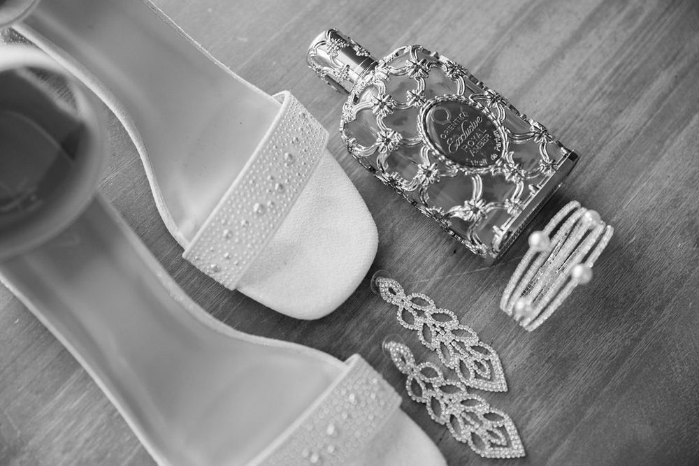 Black-and-white flat lay of rhinestone sandals, an ornate perfume bottle, chandelier earrings and a pearl cuff