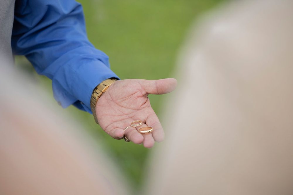 Officiant in a blue shirt holding the two gold wedding bands in his open palm