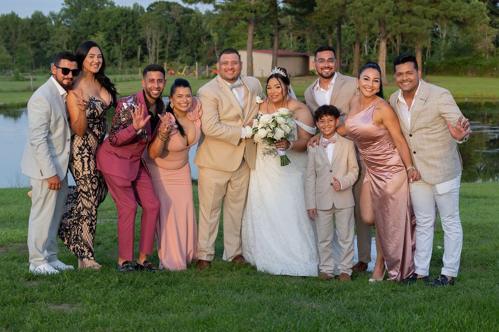 Bride and groom with friends and a young boy in a matching tan suit posing by a pond at golden hour
