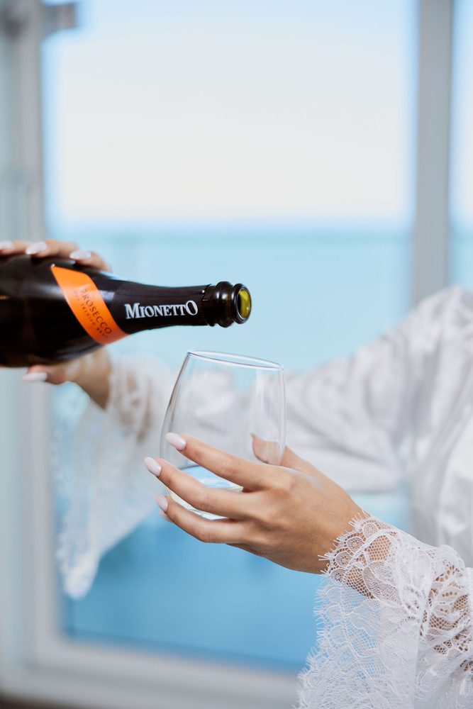 Close-up of prosecco being poured into a stemless glass held by a hand in a lace-trimmed sleeve
