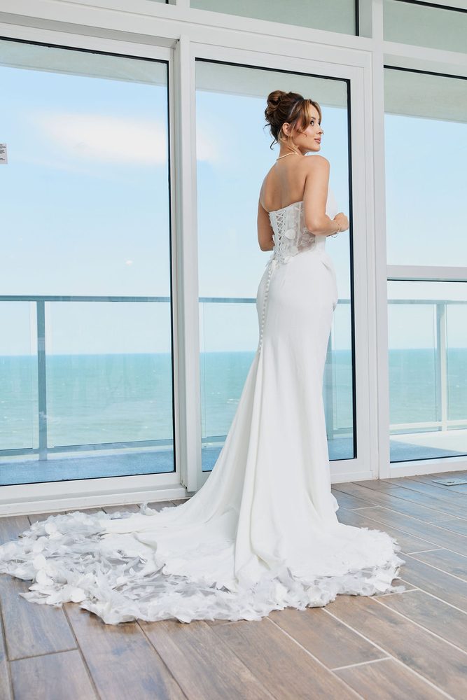 Bride glancing over her shoulder in a strapless mermaid gown with lace-up back and petal train, ocean beyond