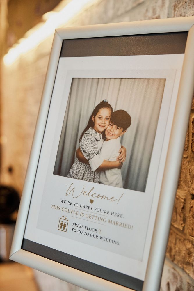 Framed welcome sign featuring a vintage childhood photo of two hugging children, directing guests to the second floor