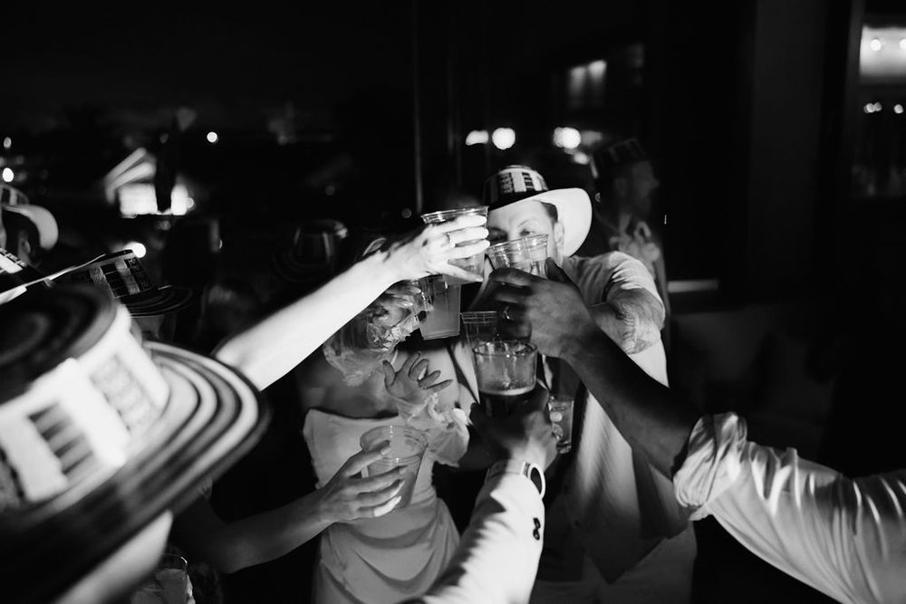 Black-and-white of the bride and guests in striped wide-brim hats clinking cups together at the late-night reception